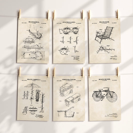 Six vintage-style beach-themed patent art prints are clipped to a white string against a sunlit wall. The prints feature black technical drawings and text for a beach sandal, aviator glasses, beach chair, beach umbrella, wheeled cooler, and beach cruiser, all on warm cream paper.