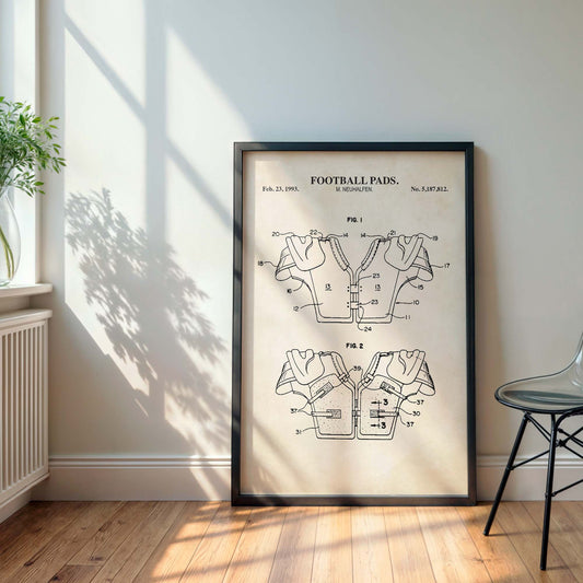 Framed poster of a football pads patent on a wall with a plant and chair in the background.