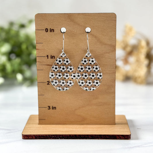 Soccer ball patterned earrings on a wooden stand with measurements.