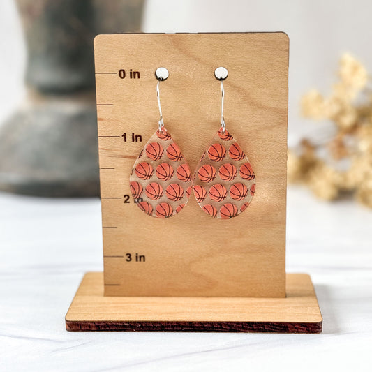 Basketball patterned earrings on a wooden stand with measurement markings.