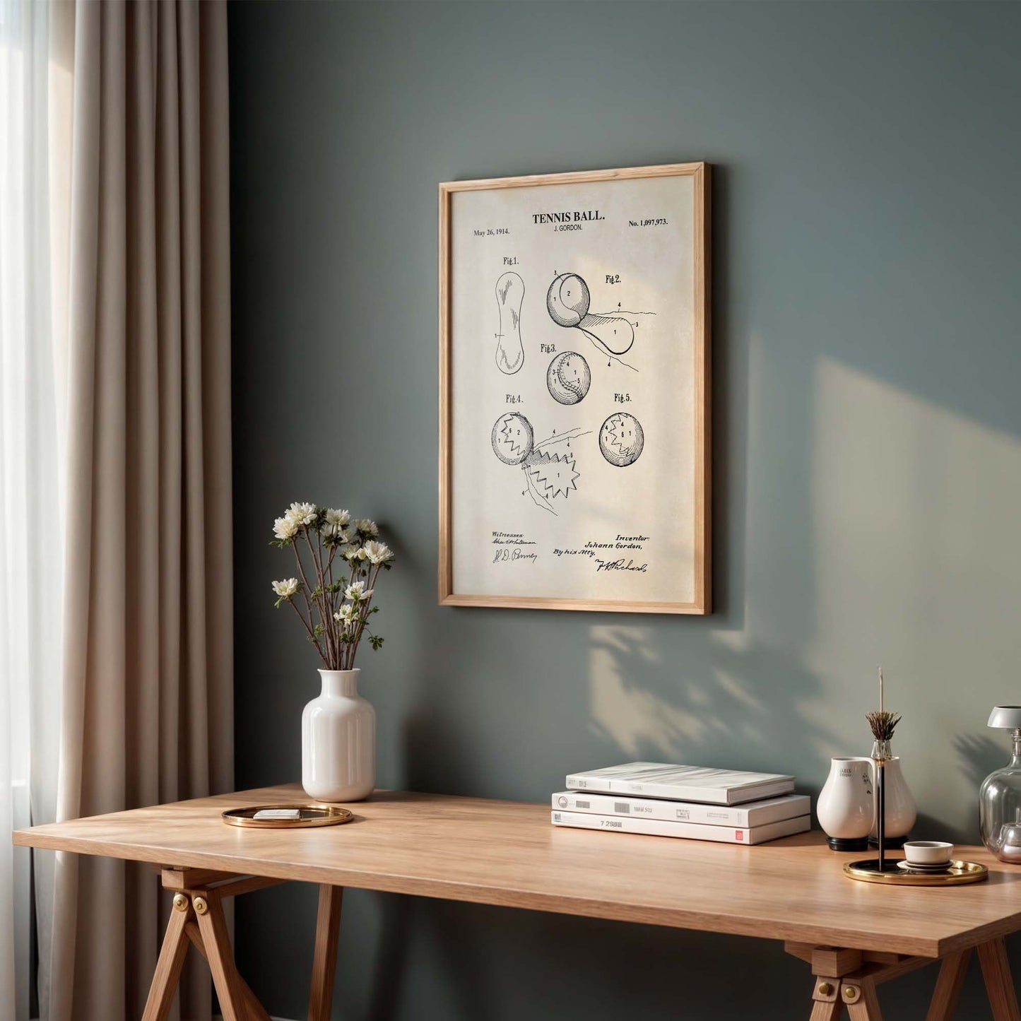 Framed tennis ball patent on a wall above a wooden desk with decor items.