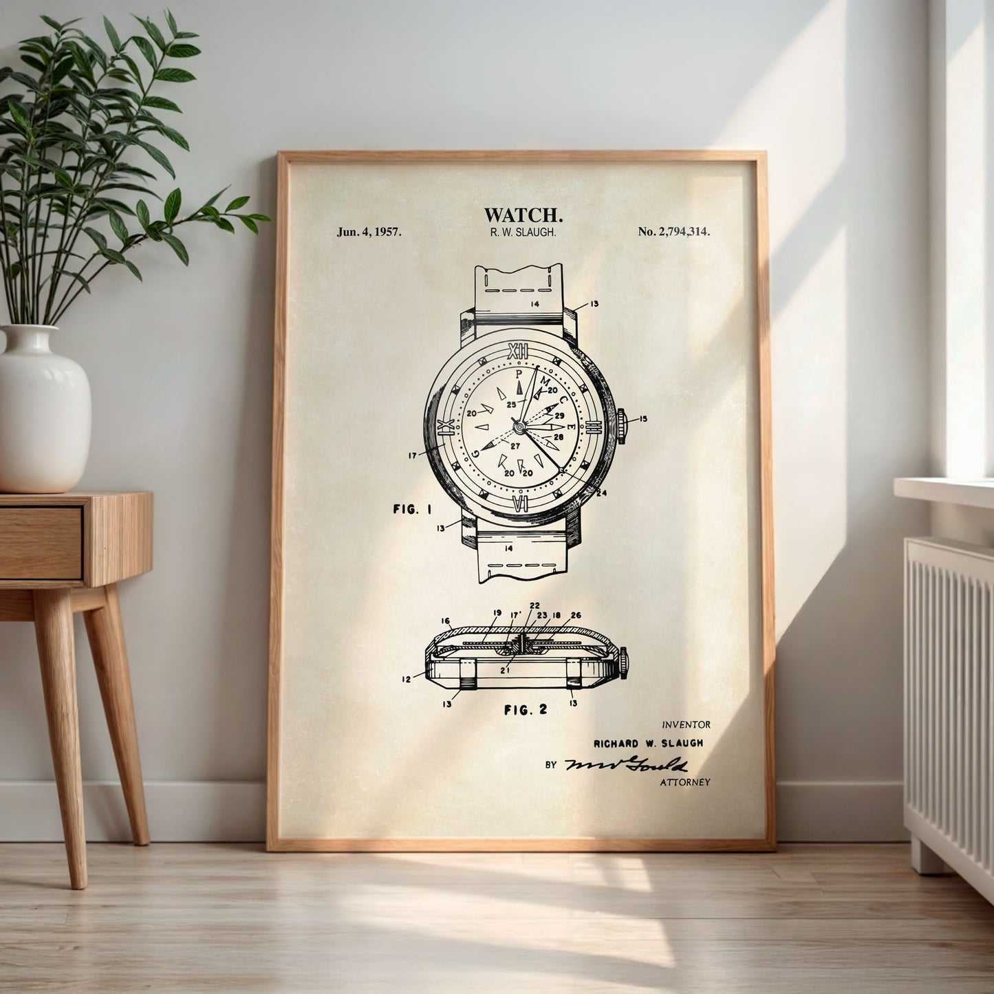 Framed watch patent print on a wall in a room with a plant and wooden side table.