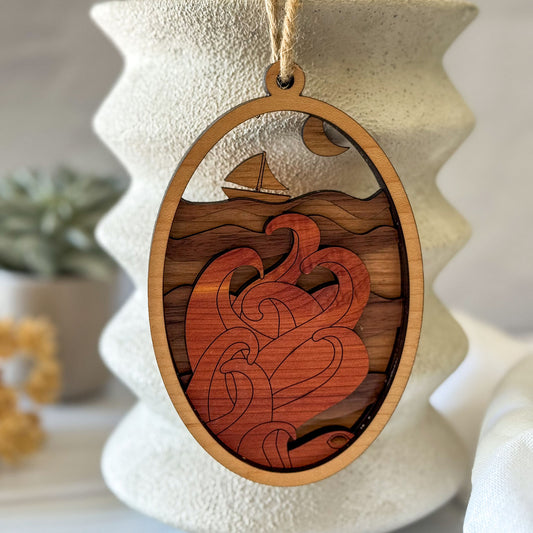 Wooden ornament with cut-out design of a sailboat and waves, hanging against a neutral background.