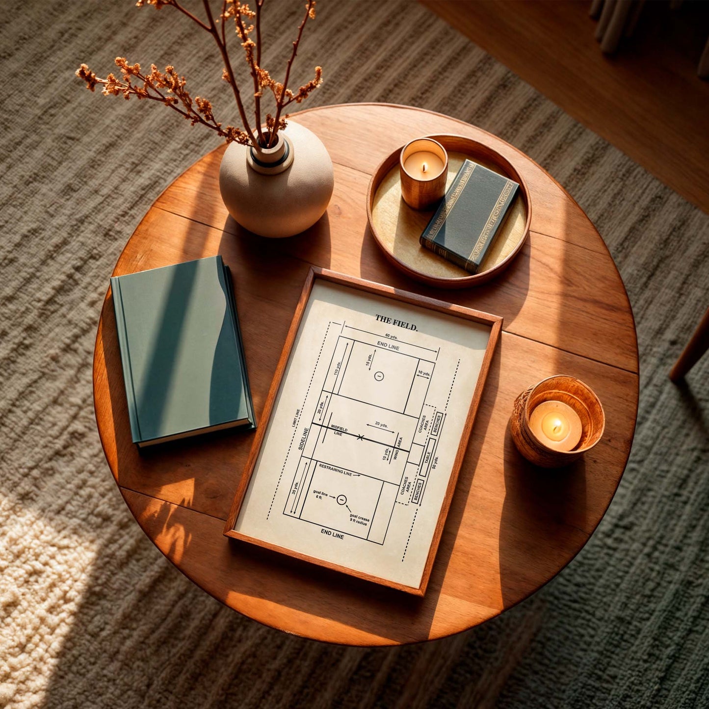 Wooden coffee table with books, candles, and a framed men's lacrosse field diagram on a textured floor.