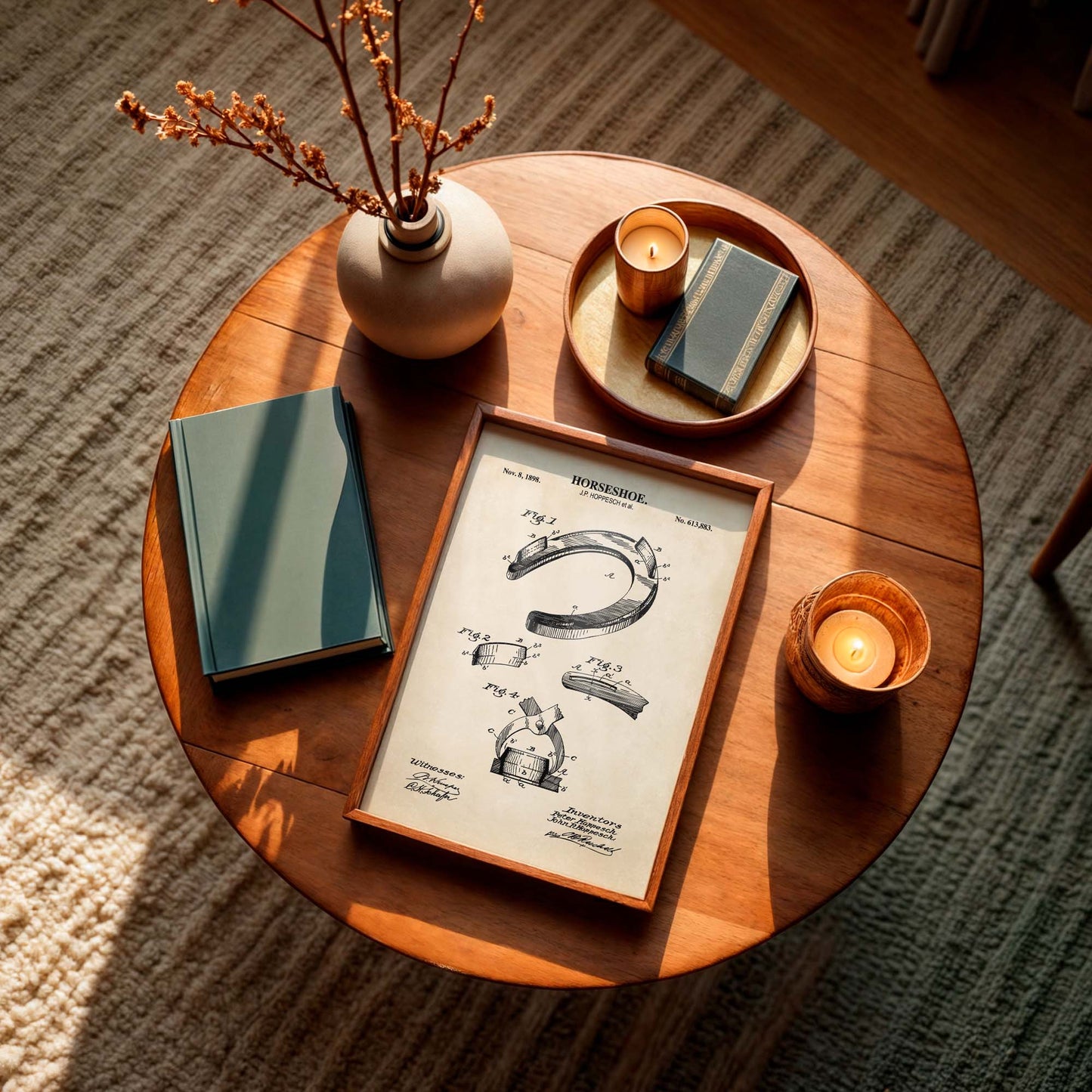 Round wooden table withframed horseshoe patent print, a vase, and candles on a textured floor.