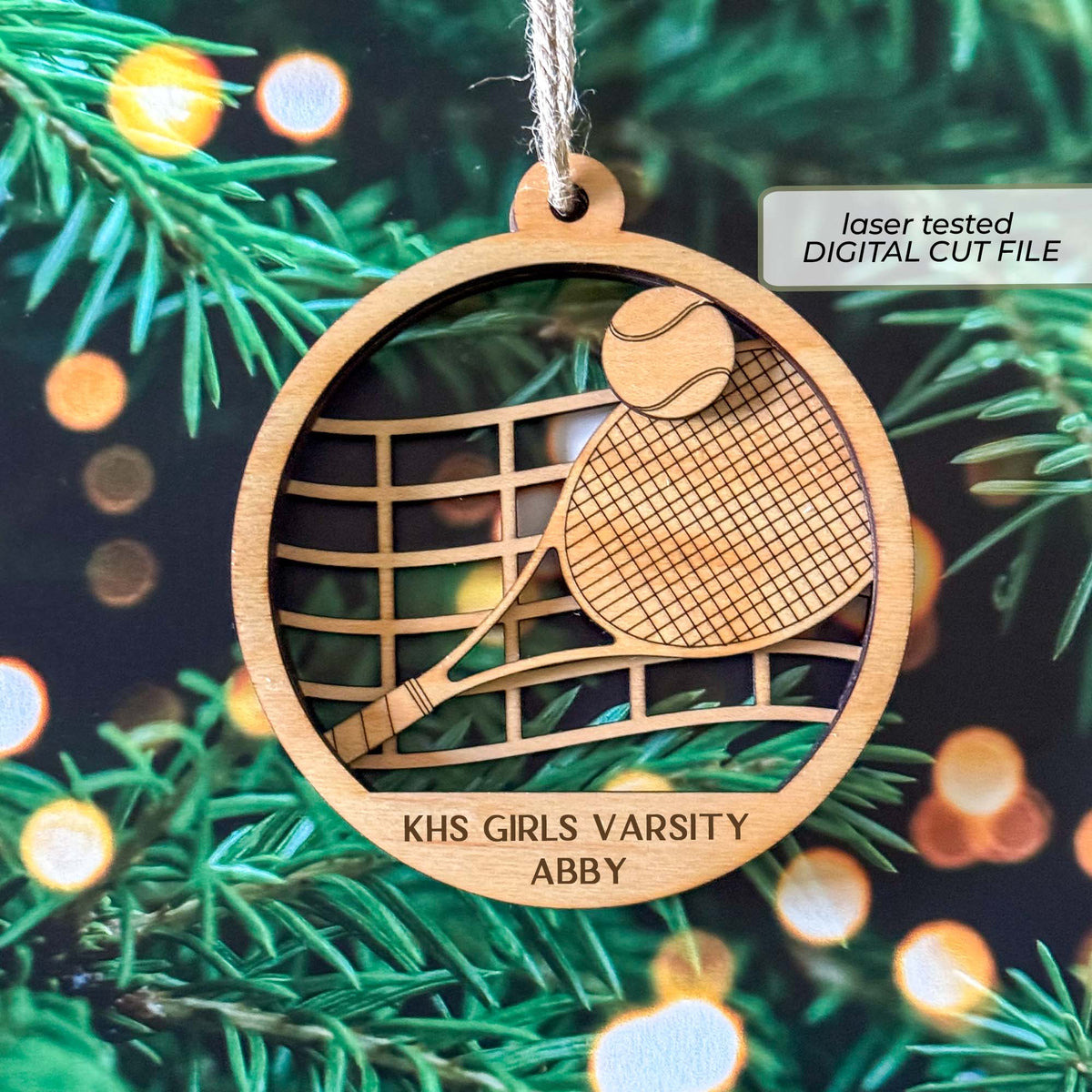 Personalized tennis ornament SVG shown as a laser-cut wooden sample with a layered racket, tennis ball, net, team name and player name.