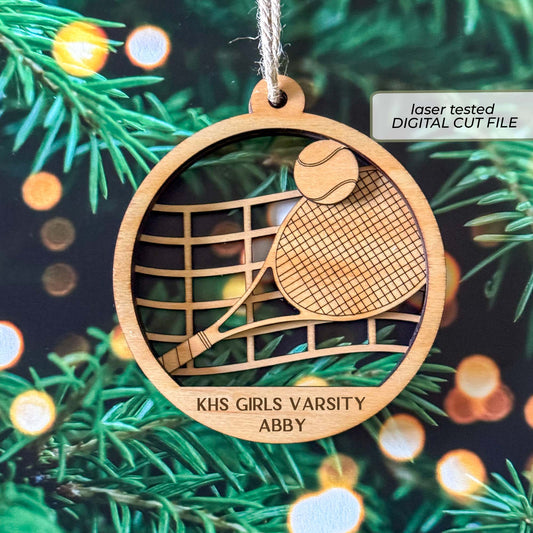 Personalized tennis ornament SVG shown as a laser-cut wooden sample with a layered racket, tennis ball, net, team name and player name.
