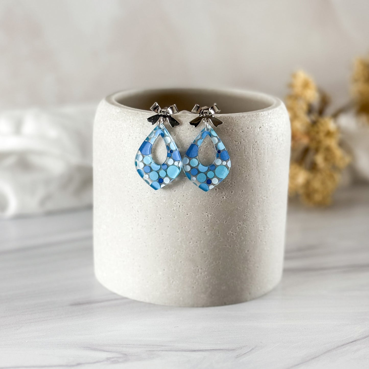 Blue teardrop earrings on a white cylindrical container with a neutral background