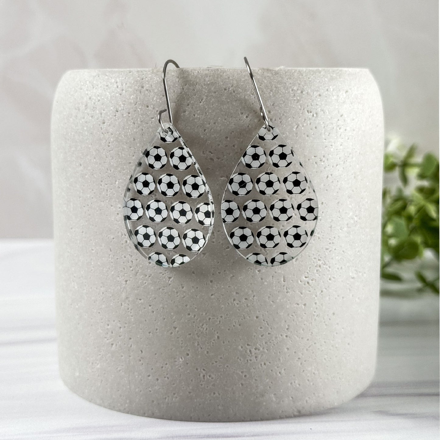 Teardrop-shaped earrings with soccer ball pattern on a white cylindrical container.