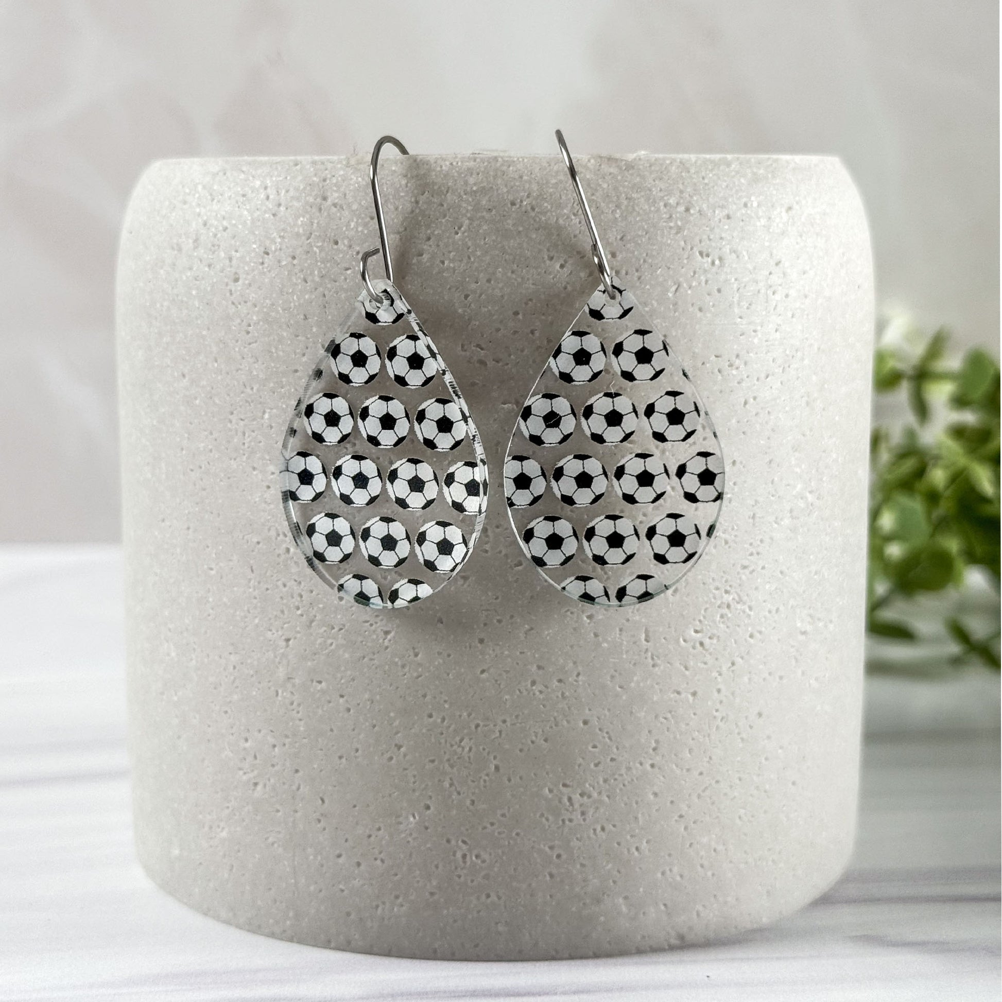 Teardrop-shaped earrings with soccer ball pattern on a white cylindrical container.
