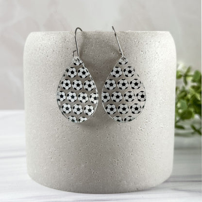 Teardrop-shaped earrings with soccer ball pattern on a white cylindrical container.