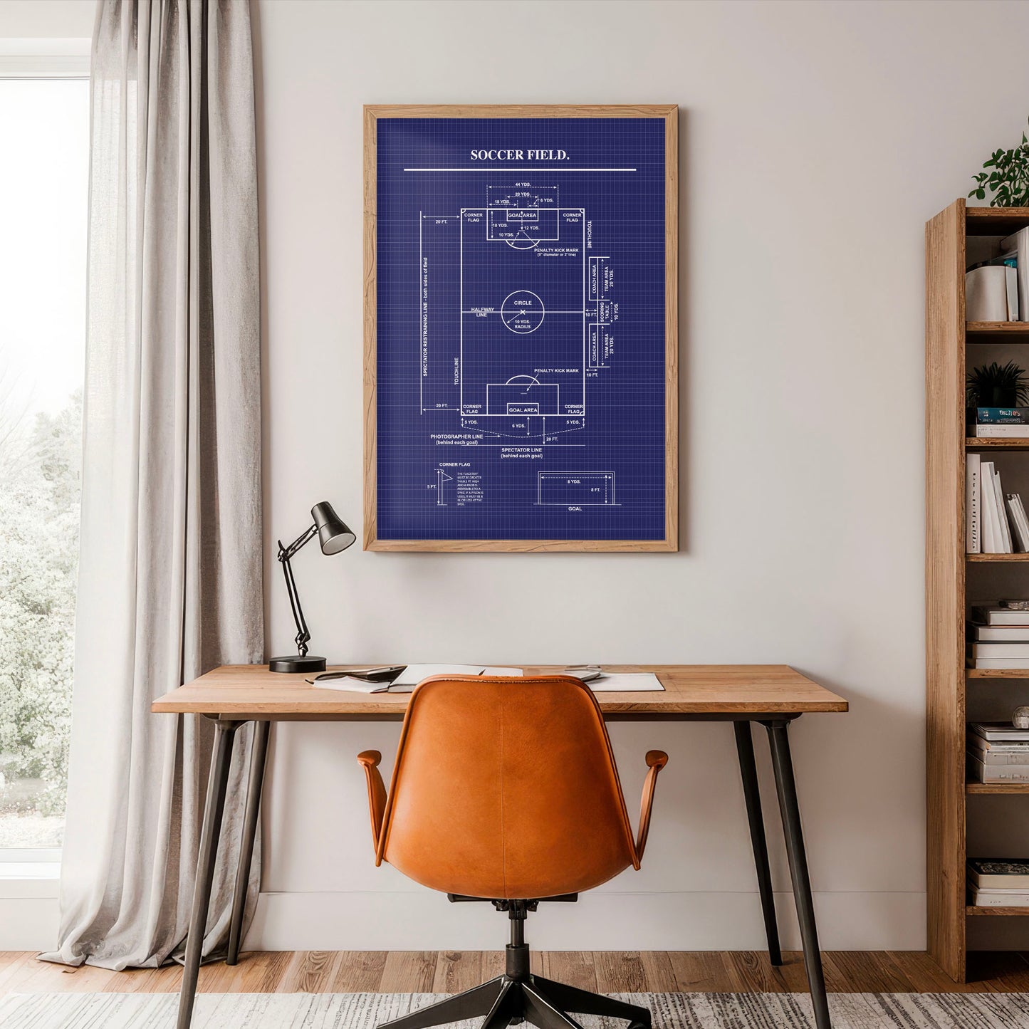 Home office with a desk, chair, lamp, and framed soccer field blueprint on the wall.