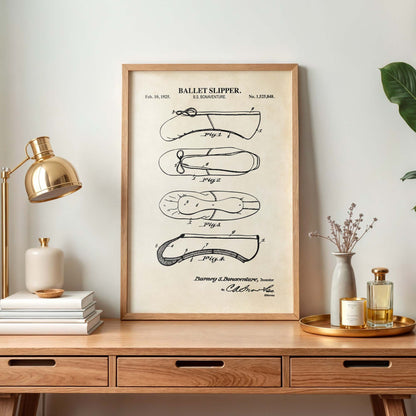 Framed ballet slipper patent print on a wooden desk with decor items.