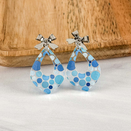 Pair of blue polka dot earrings on a light gray surface with a wooden background