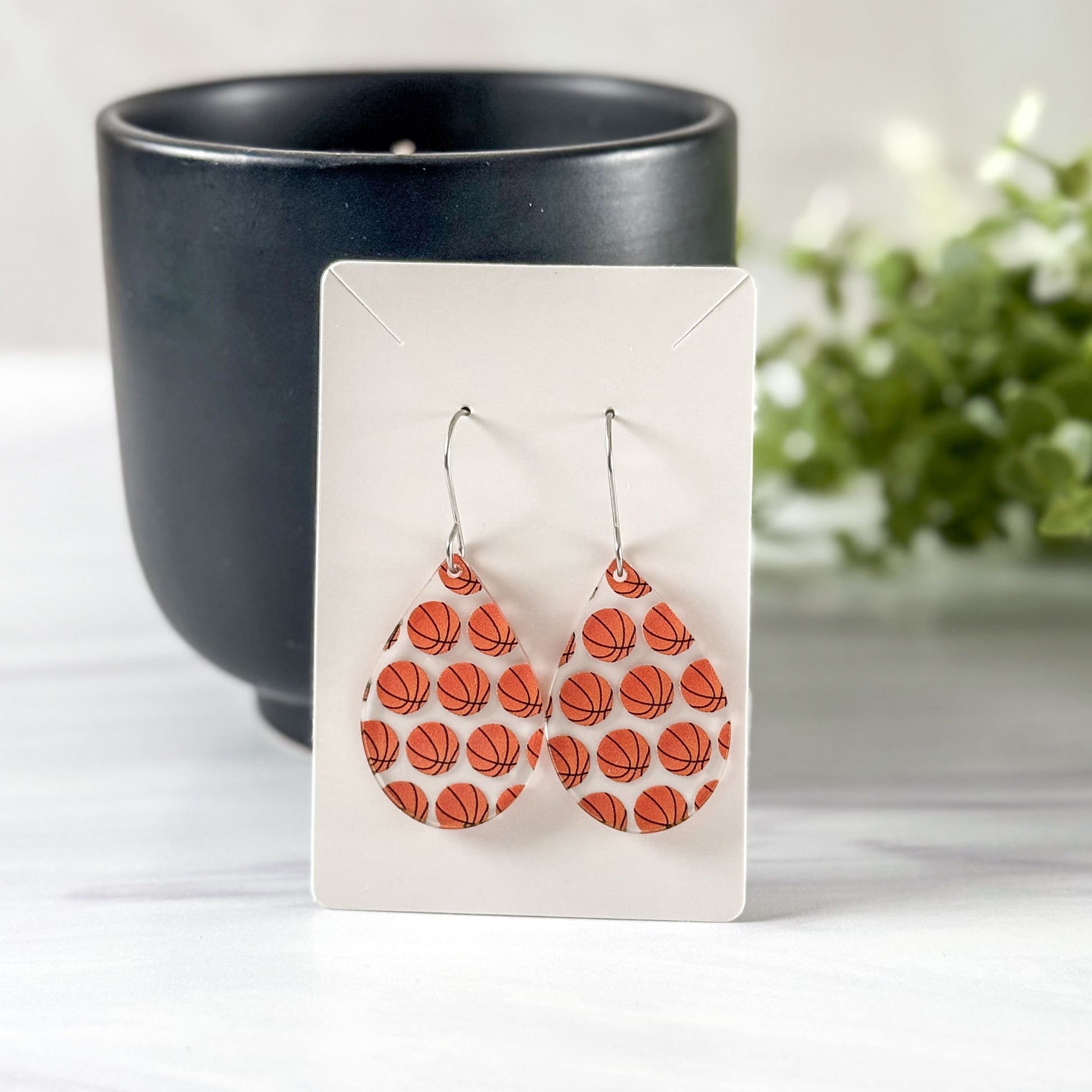 Basketball patterned earrings on a white card with a black candle and plant in the background