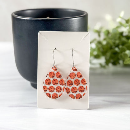 Basketball patterned earrings on a white card with a black candle and plant in the background