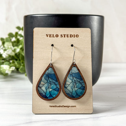 Teardrop-shaped blue earrings on a Velo Studio branded card with a black vase and greenery in the background.