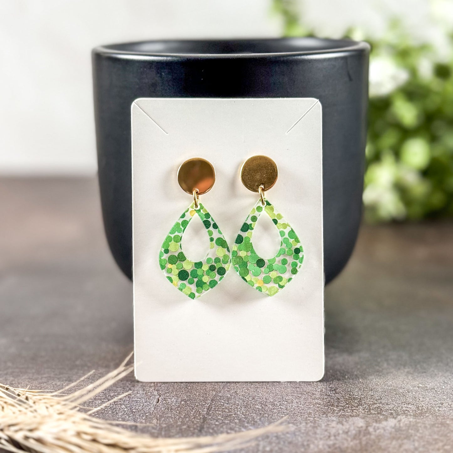 Green patterned earrings on a white card with a black cup in the background