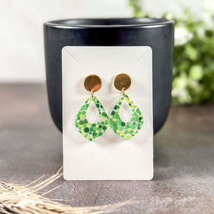 Green patterned earrings on a white card with a black cup in the background