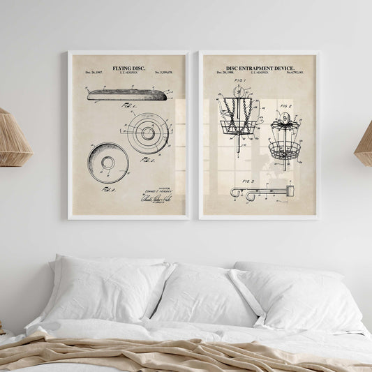 Two framed vintage patent-style wall art prints hang above a bed in a bright bedroom. The prints show technical drawings and text including 'FLYING DISC' and 'DISC ENTRAPMENT DEVICE.