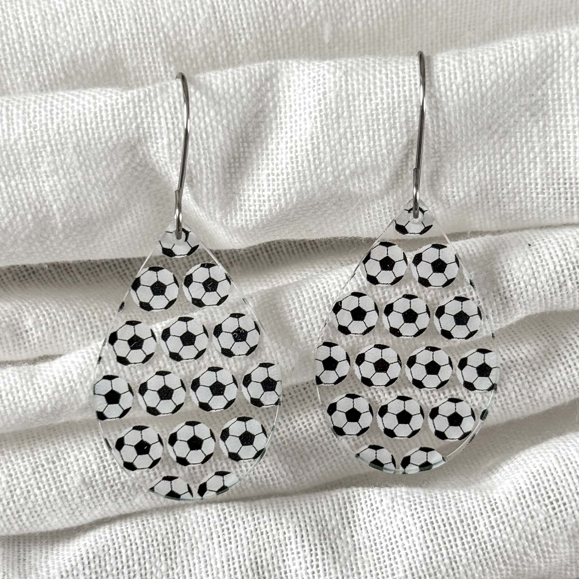 Teardrop-shaped earrings with soccer ball pattern on a white fabric background