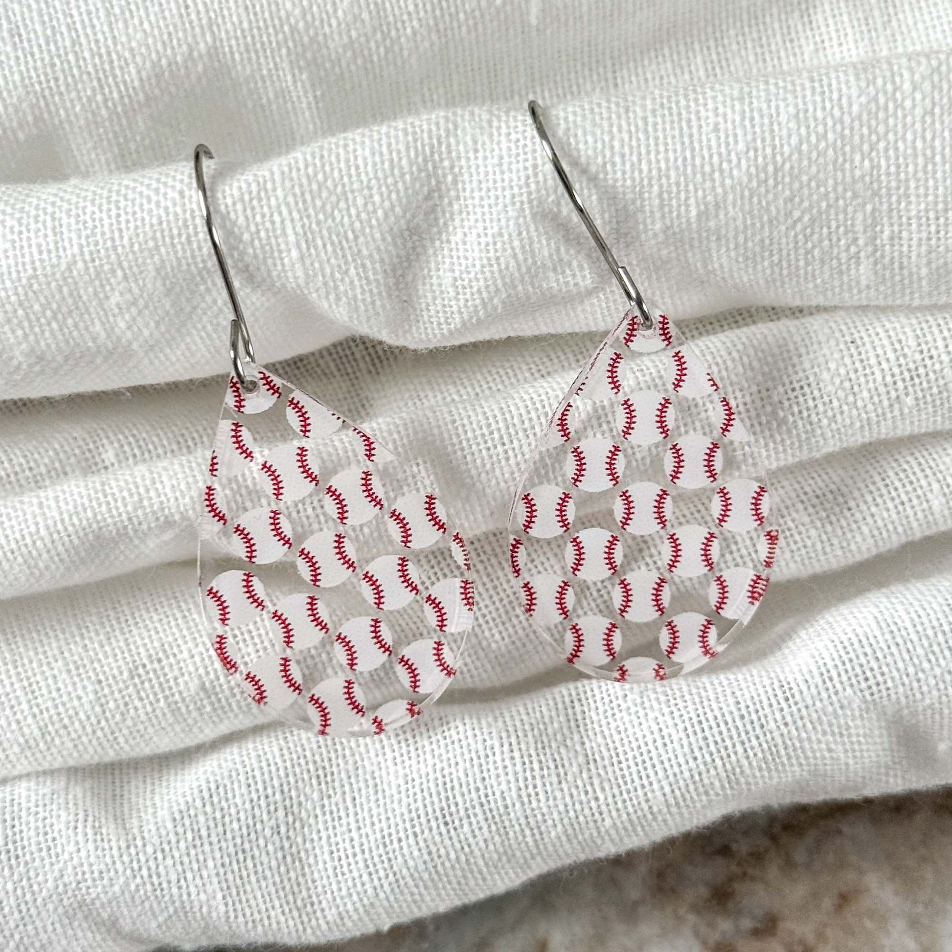 Teardrop-shaped earrings with red and white baseball pattern on a white fabric background