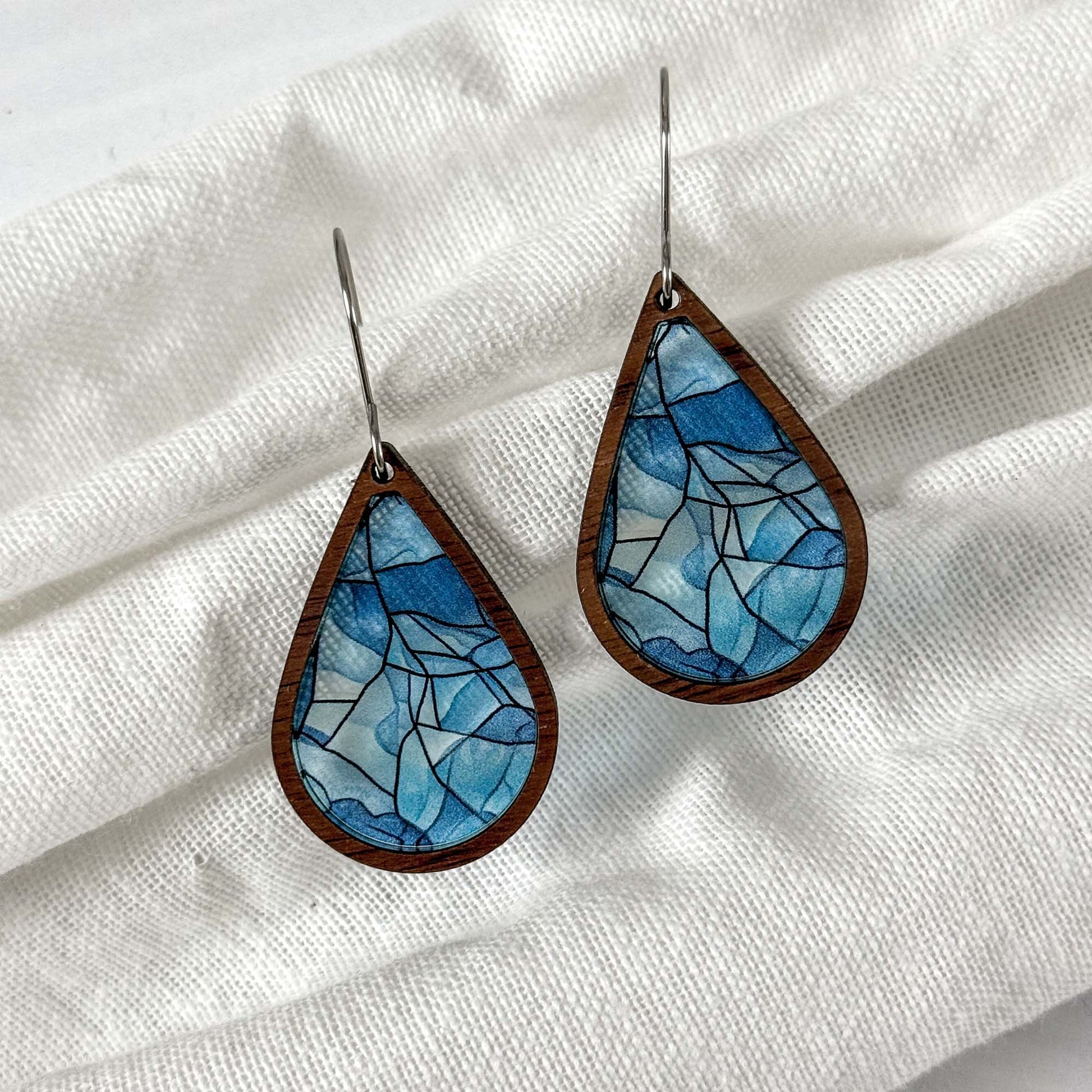 Teardrop-shaped earrings with blue mosaic design on a white fabric background