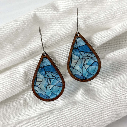 Teardrop-shaped earrings with blue mosaic design on a white fabric background