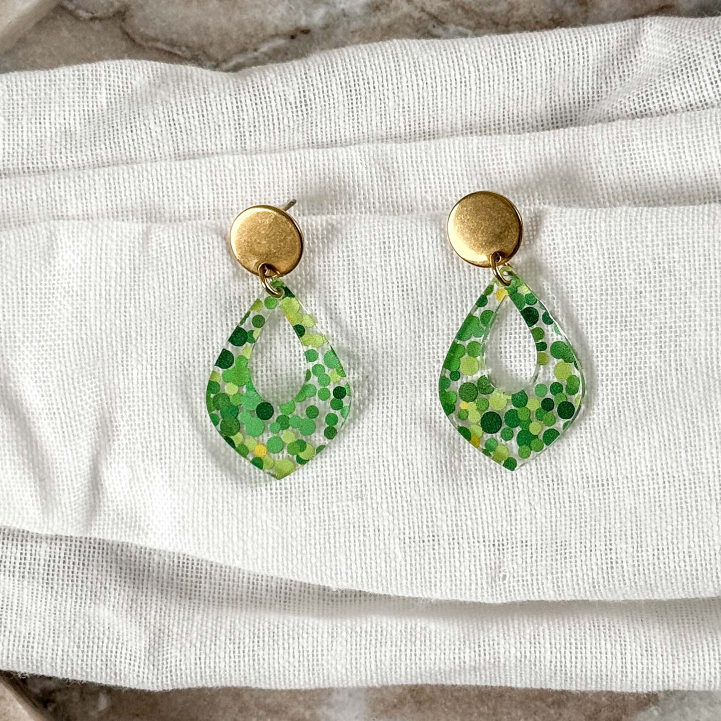 Green polka dot earrings on a white fabric background