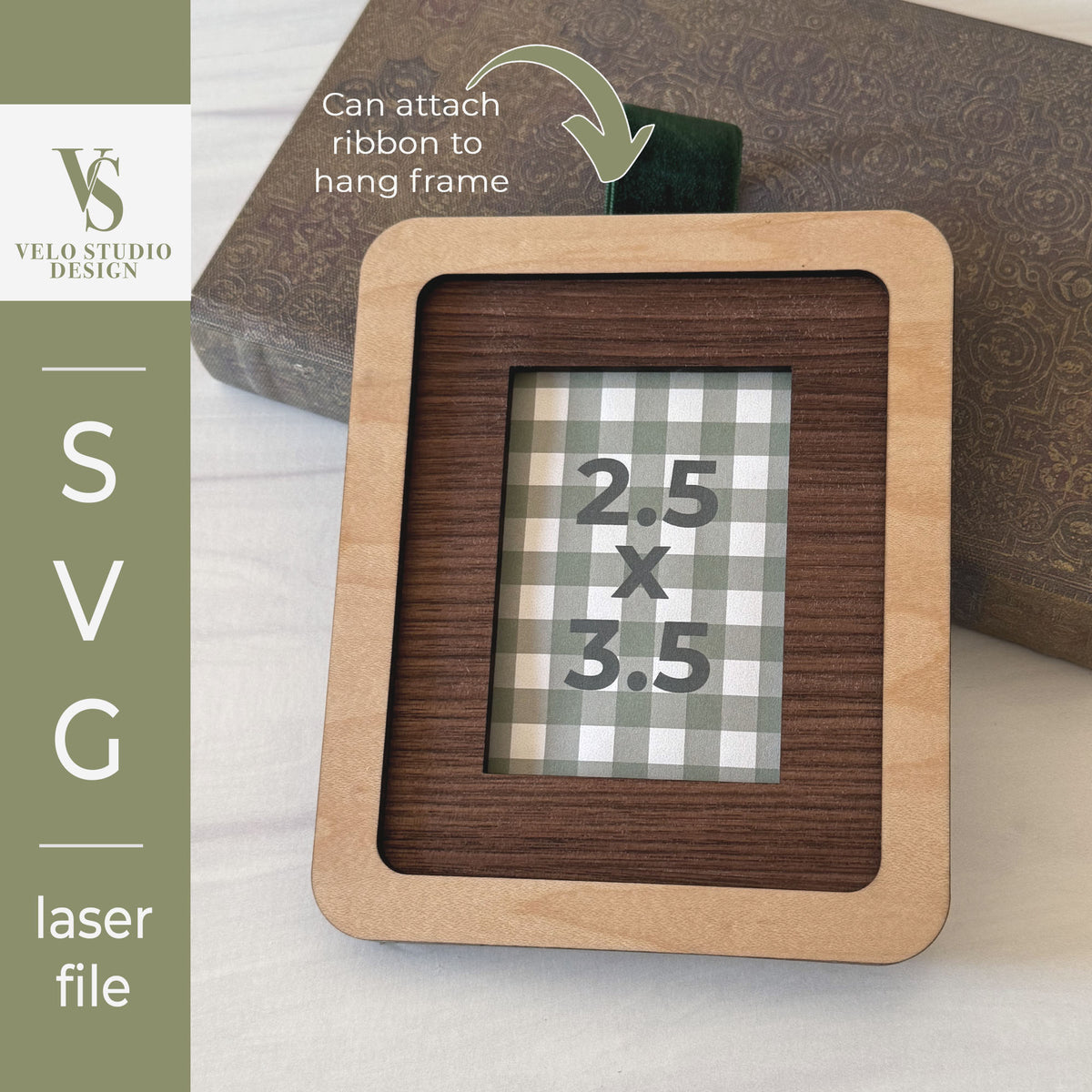 A laser-cut wooden picture frame with a light natural wood border and a darker wood inner section, shown on a tabletop with a decorative book in the background. A green ribbon is attached to the top.