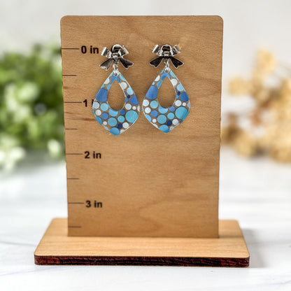 Pair of blue patterned earrings on a wooden stand with measurement markings.