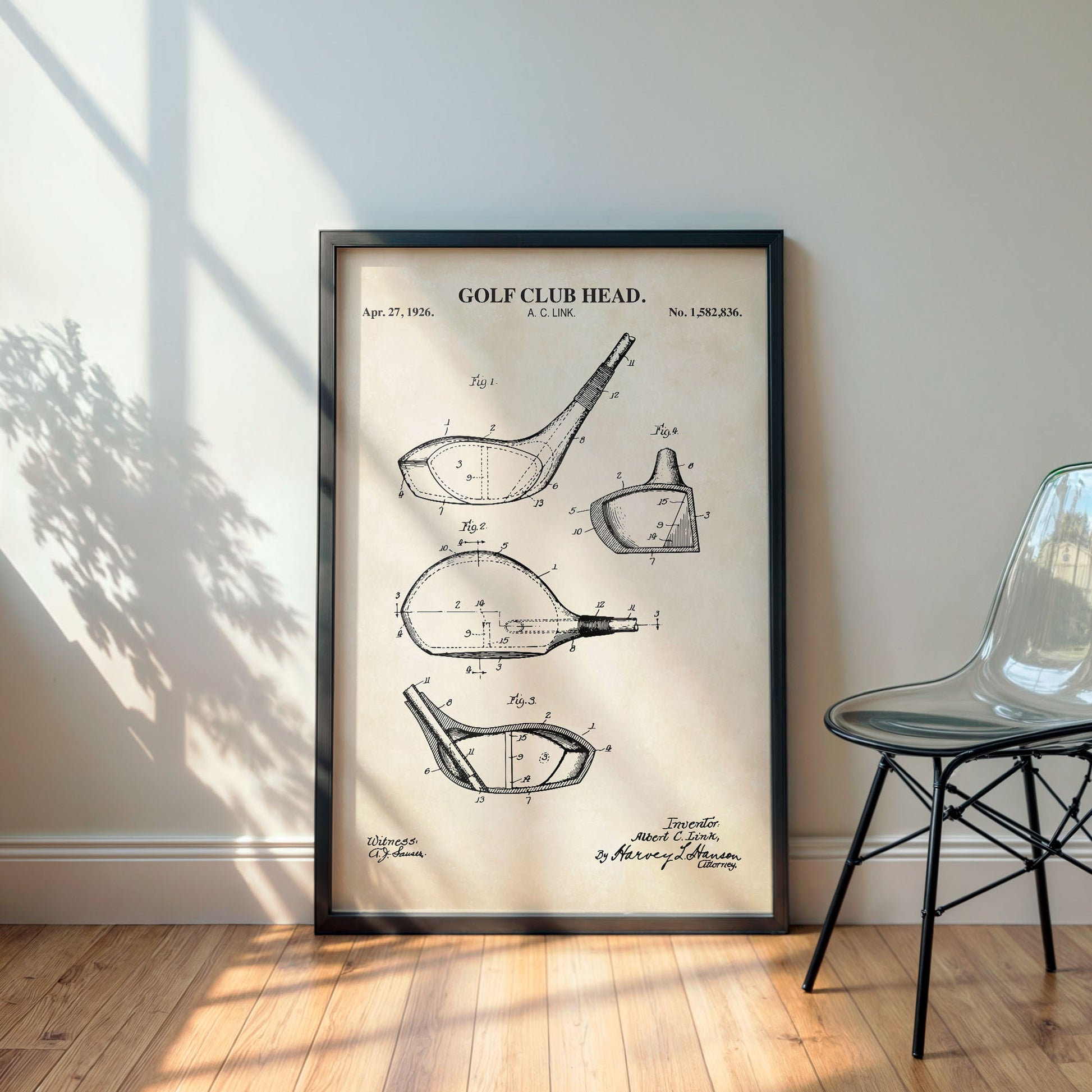 Framed golf club head patent poster on a wall with a chair and plant in the background