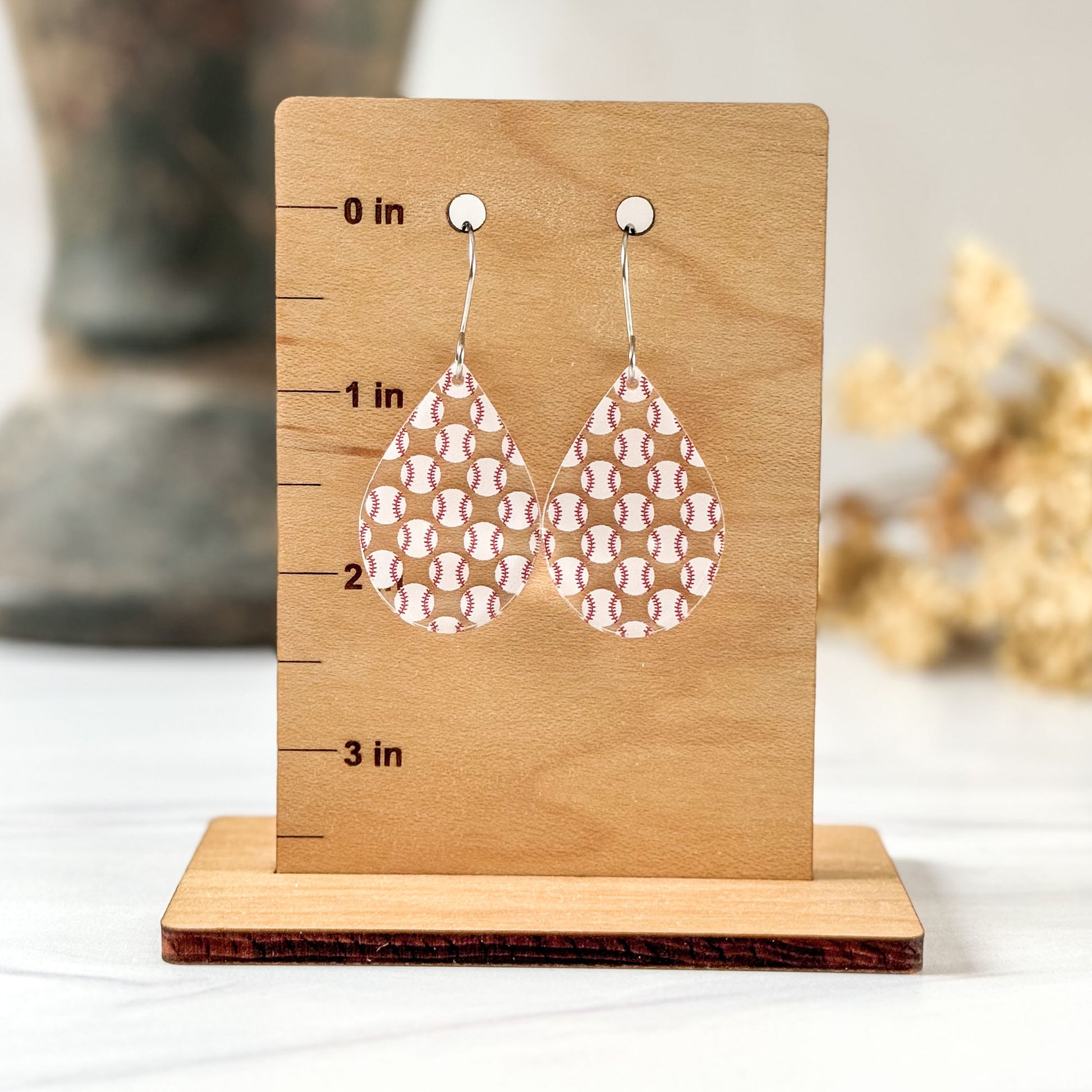 Pair of baseball patterned earrings on a wooden stand with measurements to show length of earrings.