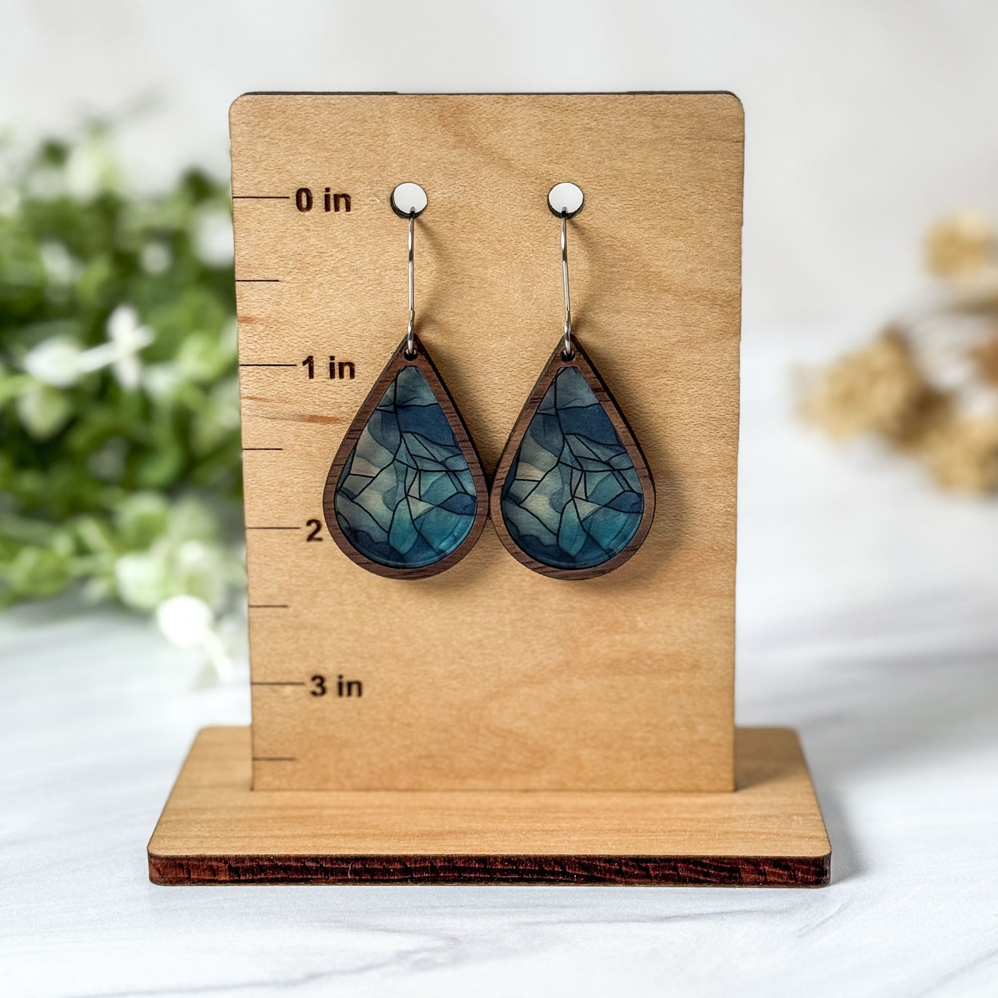 Blue teardrop earrings on a wooden stand with measurement markings.