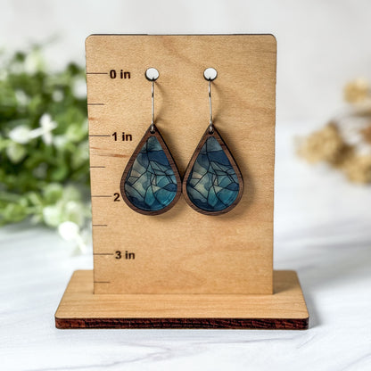 Blue teardrop earrings on a wooden stand with measurement markings.