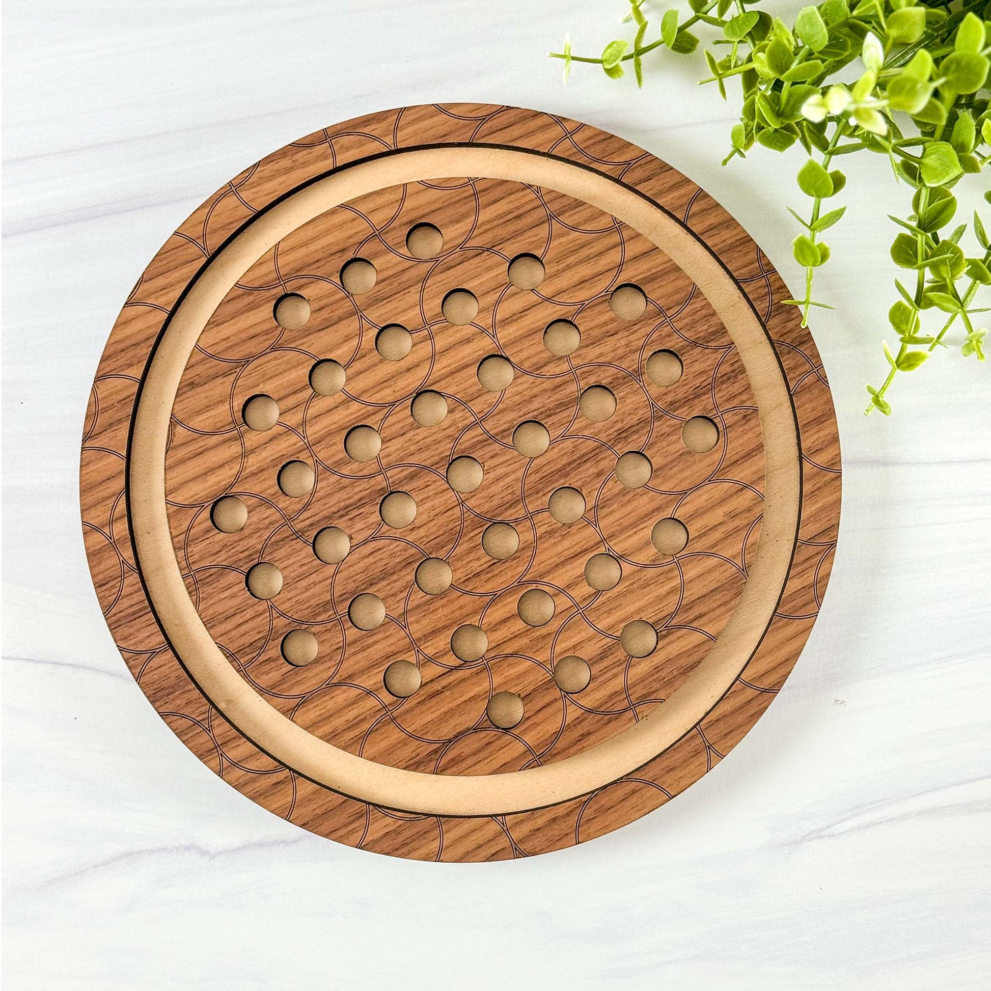 Wooden circular marble solitaire game board on a white surface with greenery.