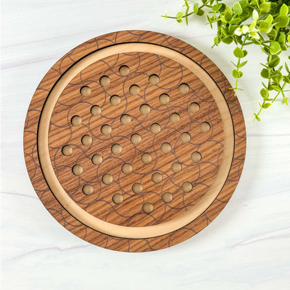 Wooden circular marble solitaire game board on a white surface with greenery.