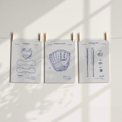 Three gray and navy baseball-themed patent art prints clipped to a string against a white wall with soft window shadows.