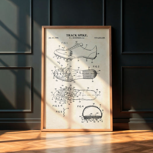 Framed patent poster of a track spike on a wooden floor with a dark paneled wall background.