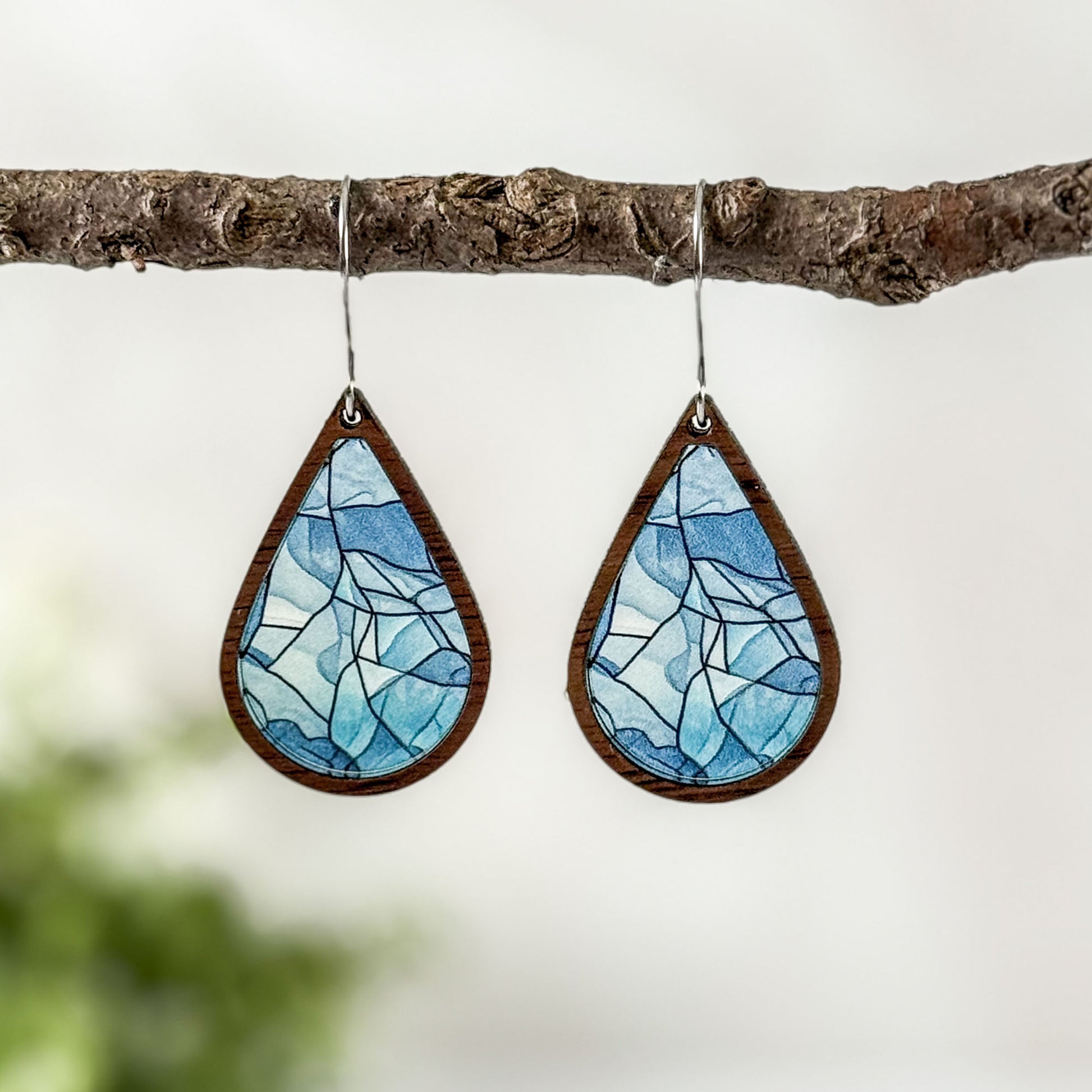 Teardrop-shaped earrings with blue mosaic design hanging on a branch.