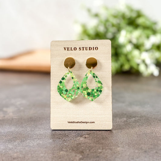 Green patterned earrings on a Velo Studio branded card with a blurred floral background.