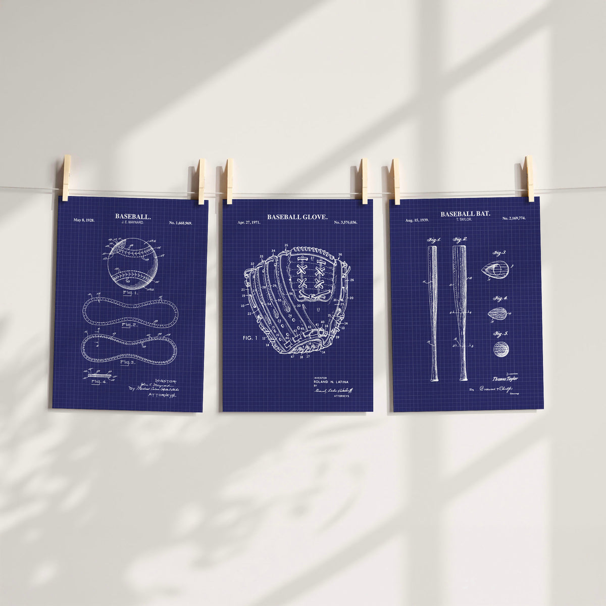Three navy blue baseball-themed patent art prints clipped to a string against a white wall with soft window shadow overlays.