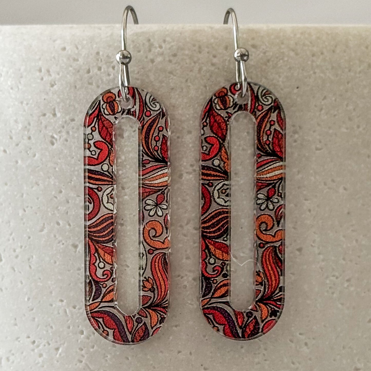 Pair of earrings with intricate red and brown pattern on a light gray background