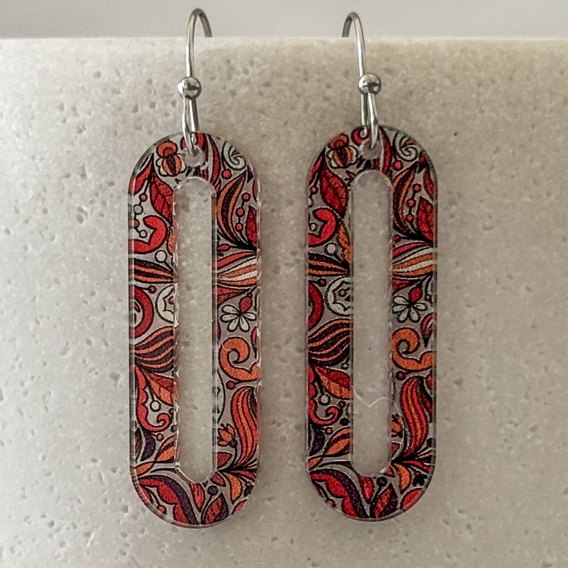 Pair of earrings with intricate red and brown pattern on a light gray background
