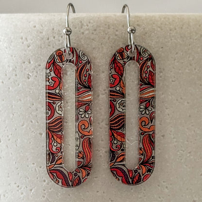 Pair of earrings with intricate red and brown pattern on a light gray background