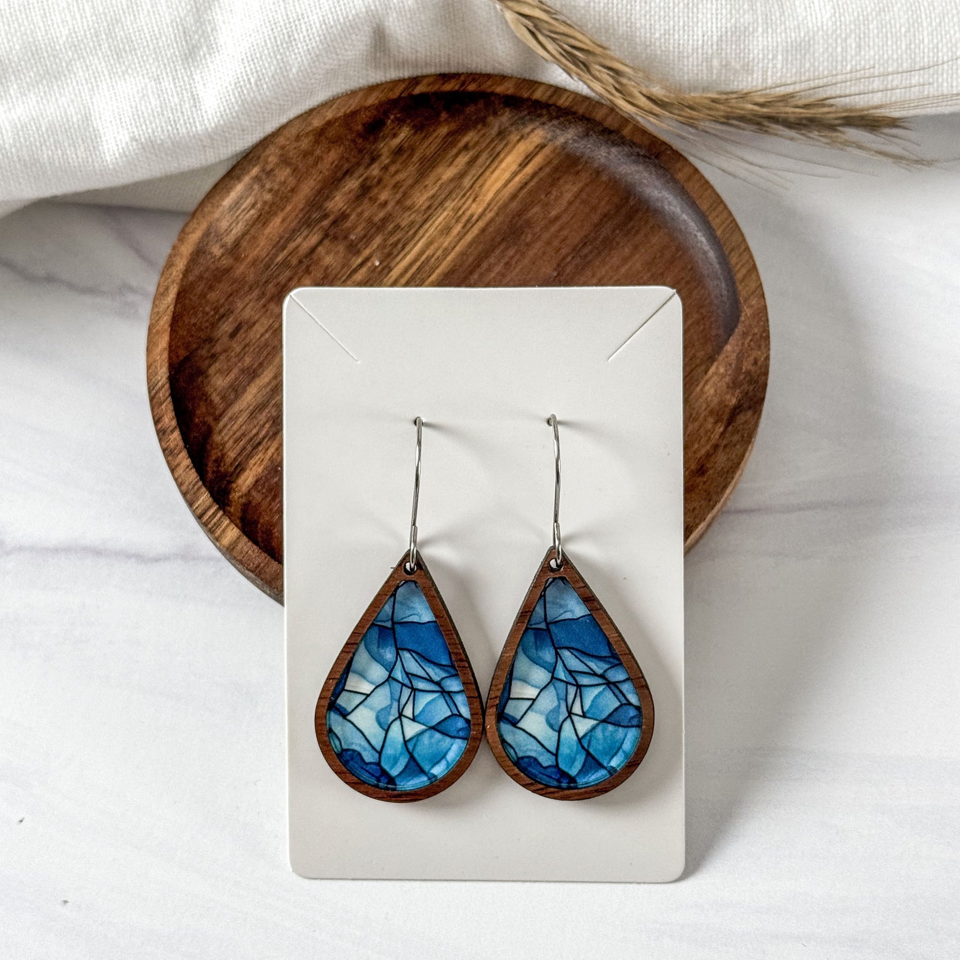 Teardrop-shaped blue mosaic earrings on a white card with a wooden base.