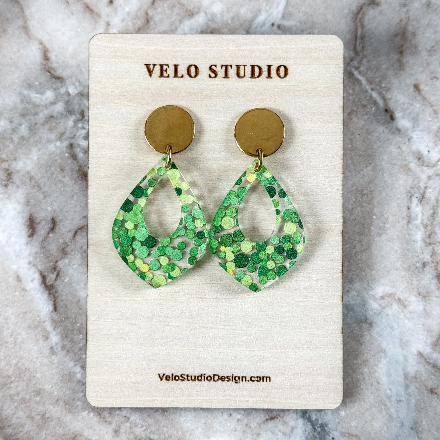 Green patterned earrings on a Velo Studio card against a marble background