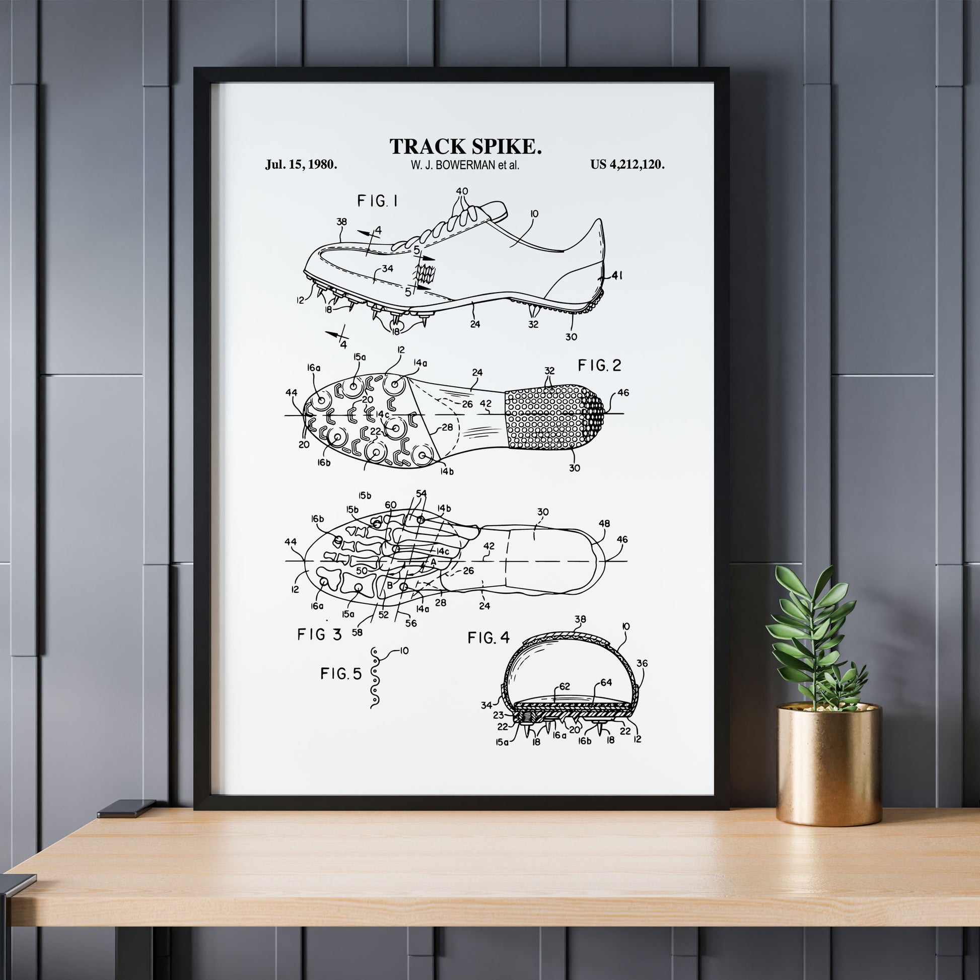Framed patent poster of a track spike on a wooden table with a plant against a gray paneled wall.