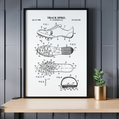 Framed patent poster of a track spike on a wooden table with a plant against a gray paneled wall.