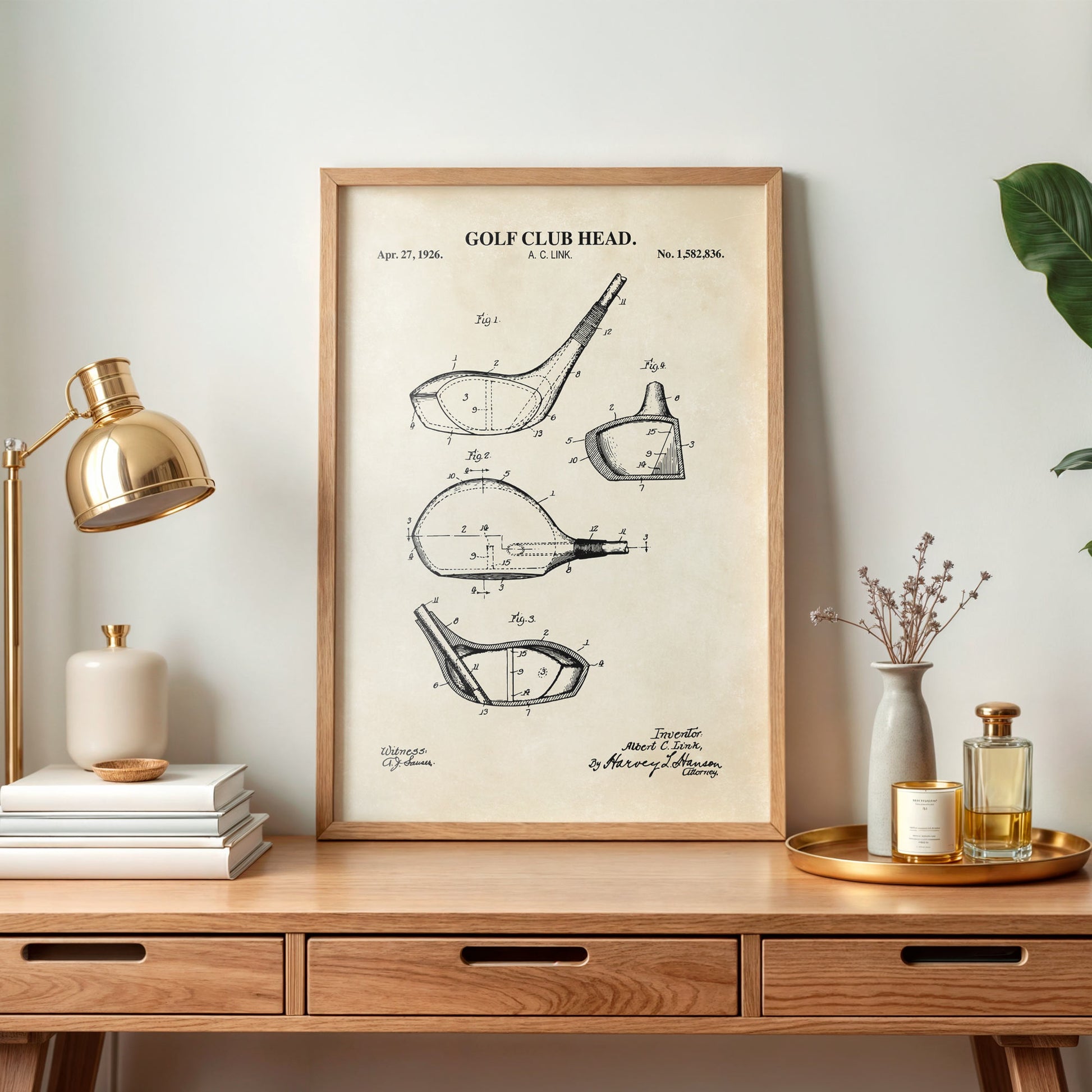 Framed golf club head patent print on a wooden desk with decor items.